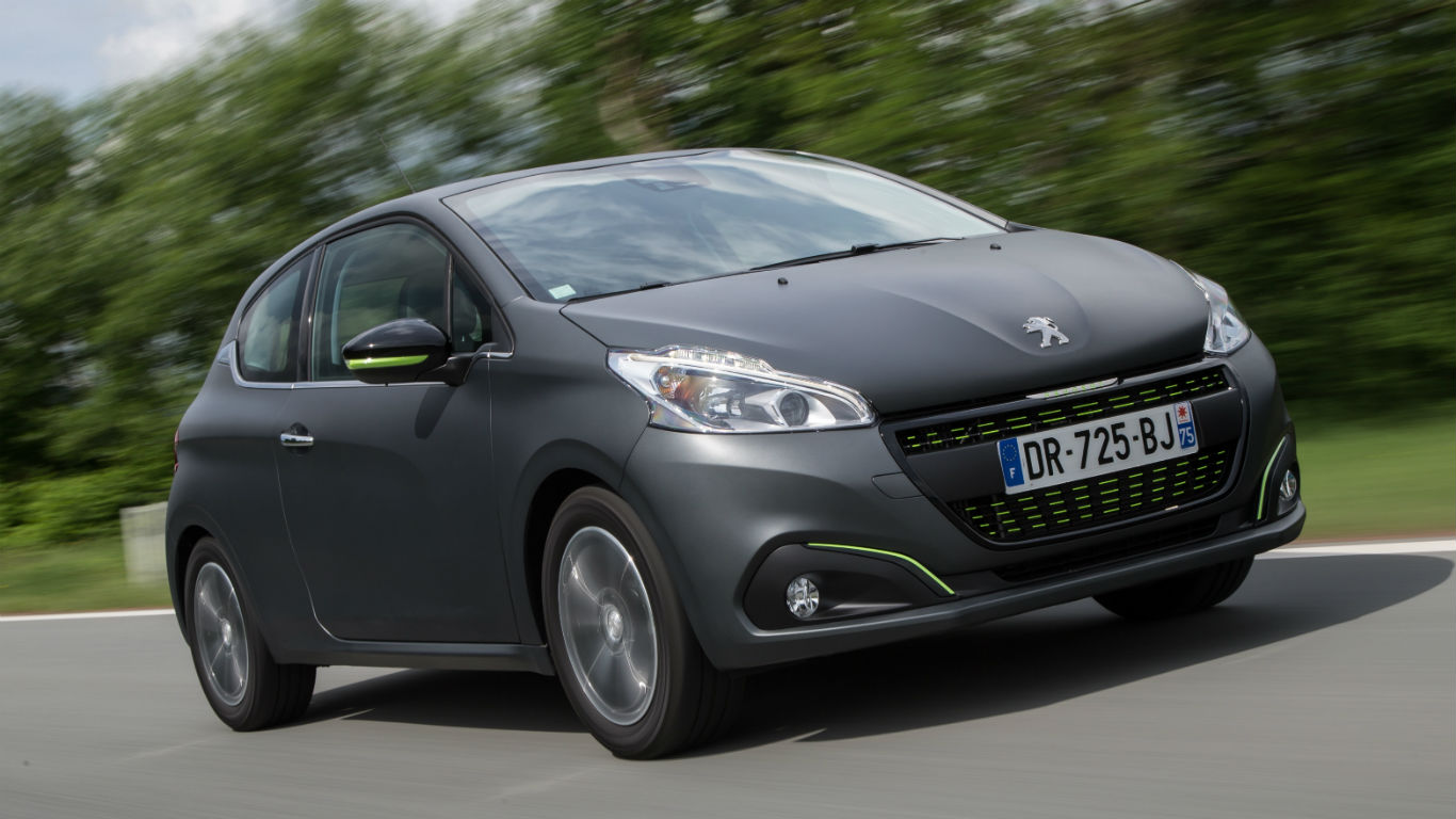 A sleek, modern Peugeot car driving on a road with blurred green trees in the background, showing motion and speed.