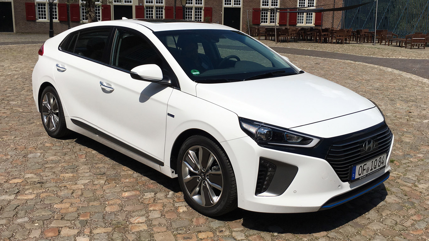 A white Hyundai car parked on cobblestone, with a red-shuttered brick building in the background.