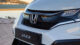 Close-up of a Honda Jazz car grille near a waterfront, with a blurred cityscape in the background, under clear skies.