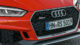 Close-up of a red Audi RS5 front grille showcasing logo, license plate, and sleek design details on a textured ground.