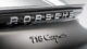 Close-up of a Porsche 718 Cayman badge on a glossy car surface, highlighting the brand logo with reflective chrome lettering.