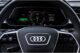 Close-up of an Audi digital dashboard displaying speed, range, and date. Steering wheel with logo is visible in foreground.