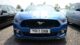 A blue Ford Mustang with white stripes parked between two cars in a lot, featuring a front grille emblem and UK license plate.
