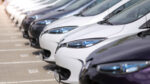 Row of parked cars lined up closely, focusing on front sections and headlights, with a blurred background and no people visible.