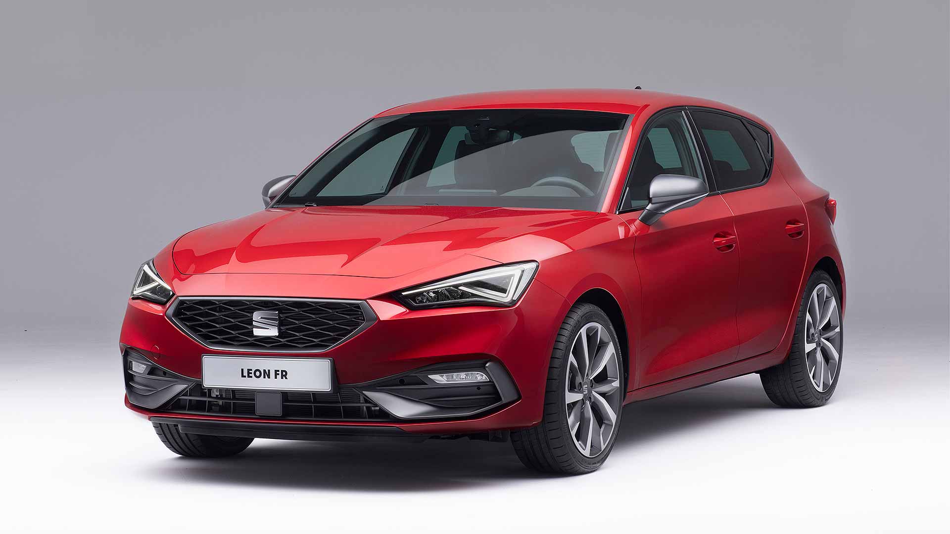 A red SEAT Leon FR car is displayed in a studio setting with a neutral gray background, showcasing its modern design.