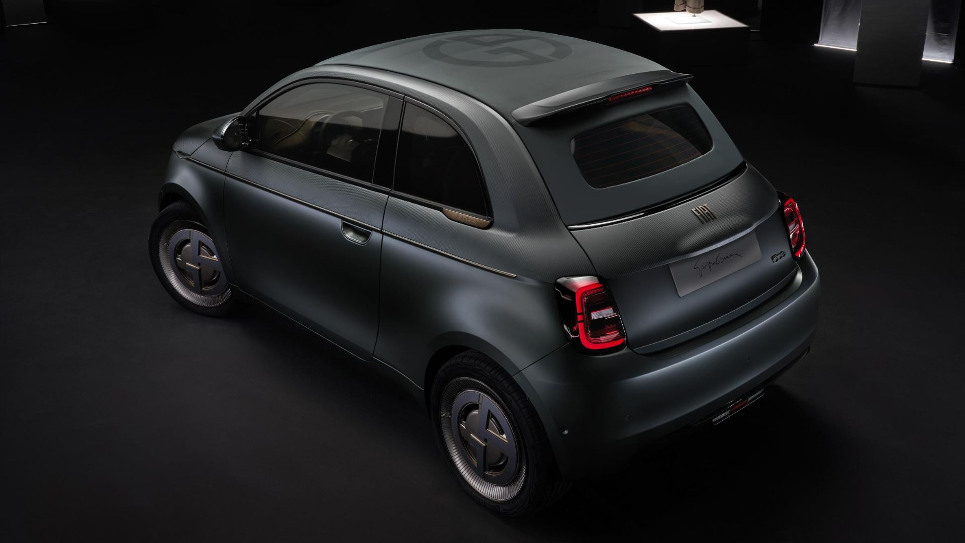 A sleek green Fiat car with custom rims and signature on the back, displayed under soft spotlight in a dark room.