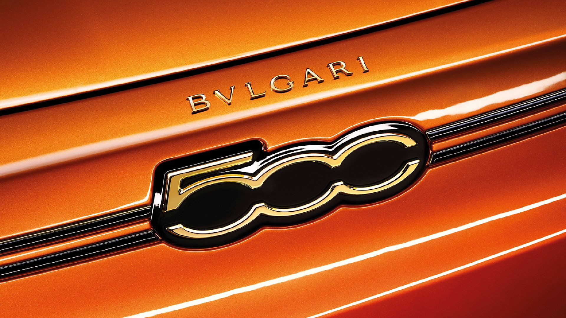 Close-up of an orange car with "BVLGARI" branding and gold-accented "500" emblem on the front. Sleek, luxurious design detail.