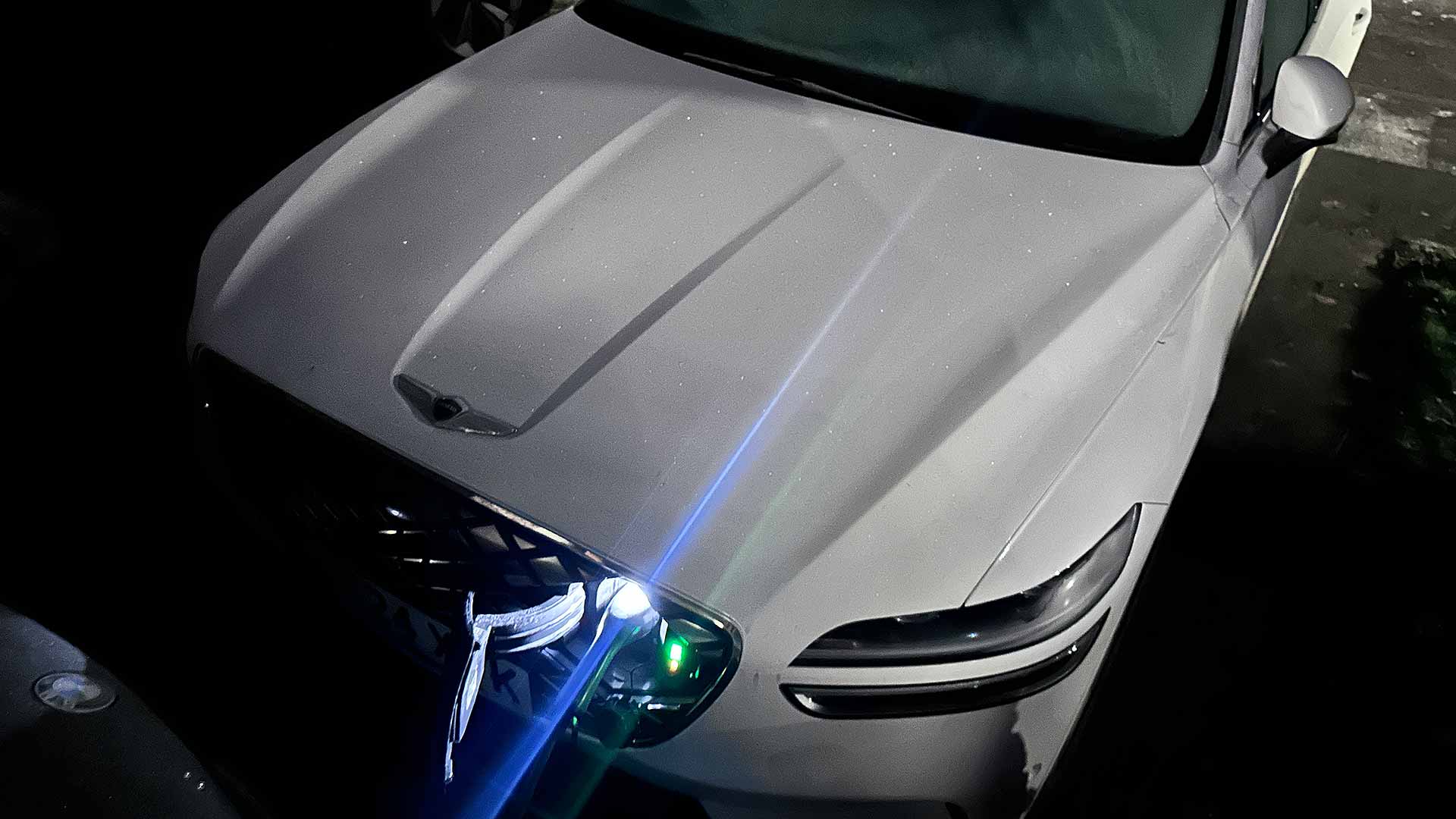 A white car with tape on the grille and headlights, parked at night. Slight reflections visible on the surface.