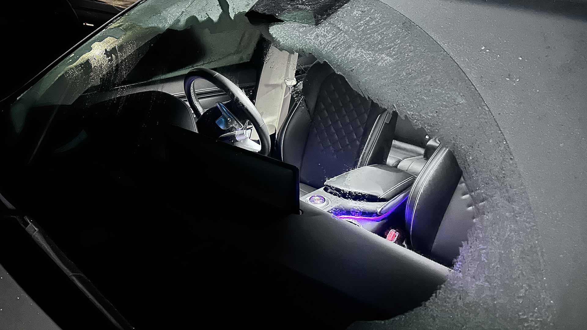 A car interior is visible through a broken ice-covered windshield, showing leather seats and dashboard illumination.