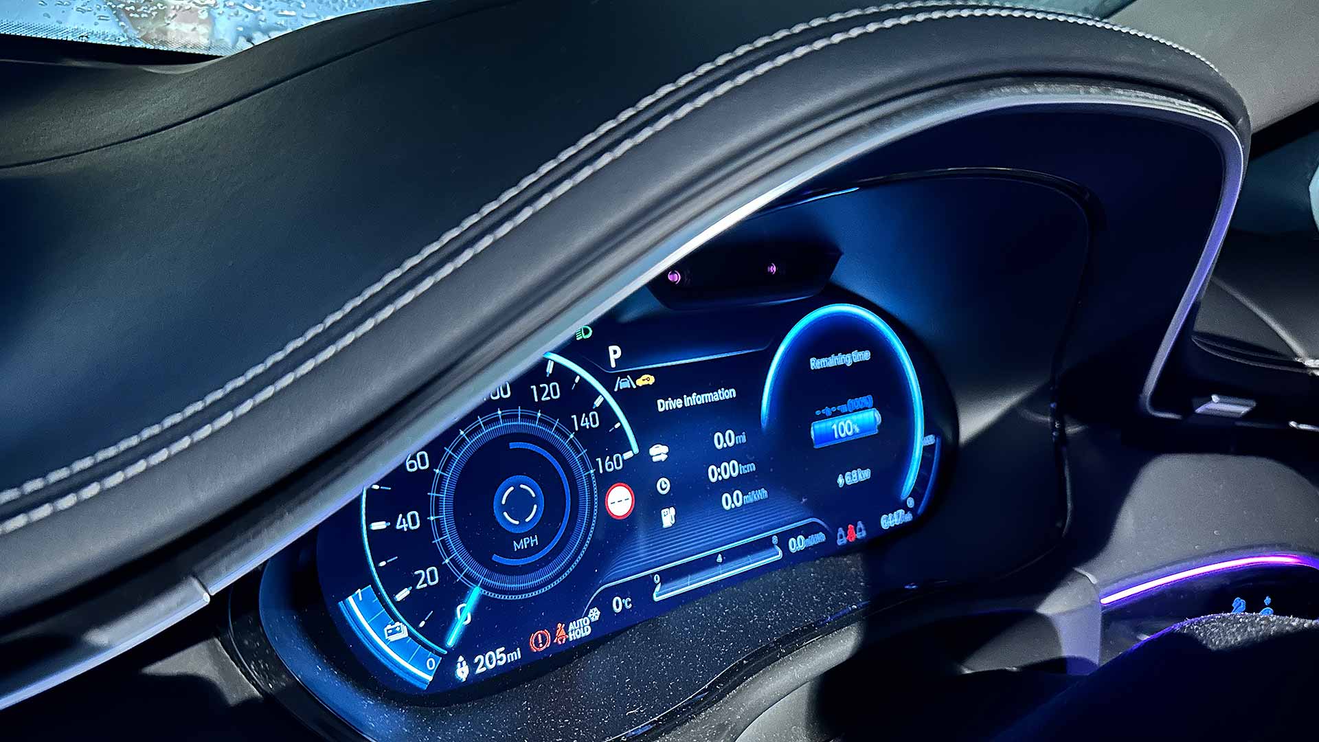Close-up of a car dashboard displaying speedometer, range, and drive information in a sleek, futuristic design with ambient purple lighting.