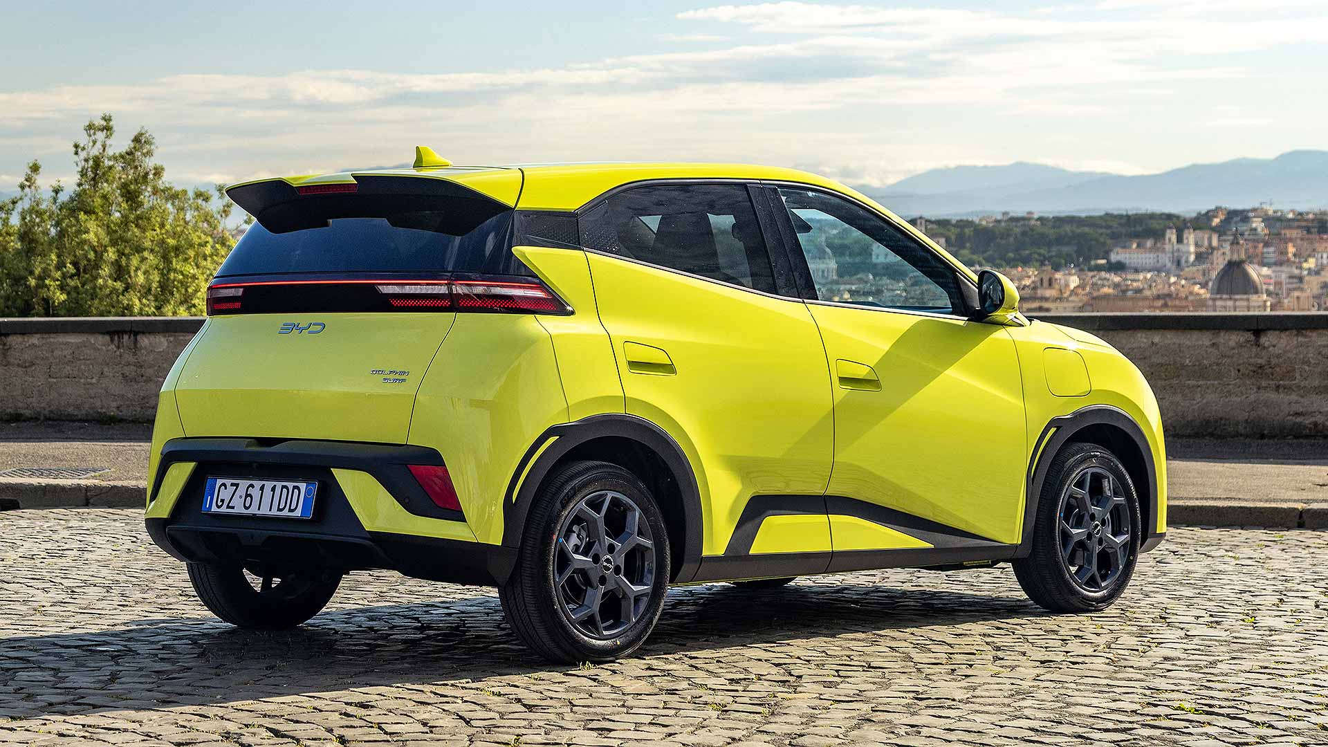Bright yellow car parked on cobblestone ground, overlooking a cityscape with iconic dome of Florence Cathedral visible in the background.
