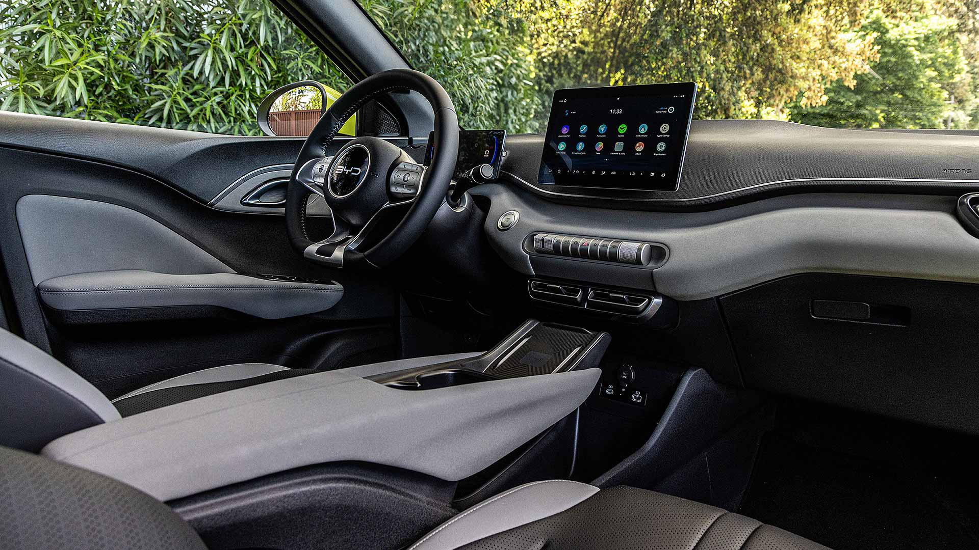 Modern car interior with sleek dashboard, touchscreen display, and ergonomic design. Lush greenery visible outside, creating a stylish and inviting atmosphere.