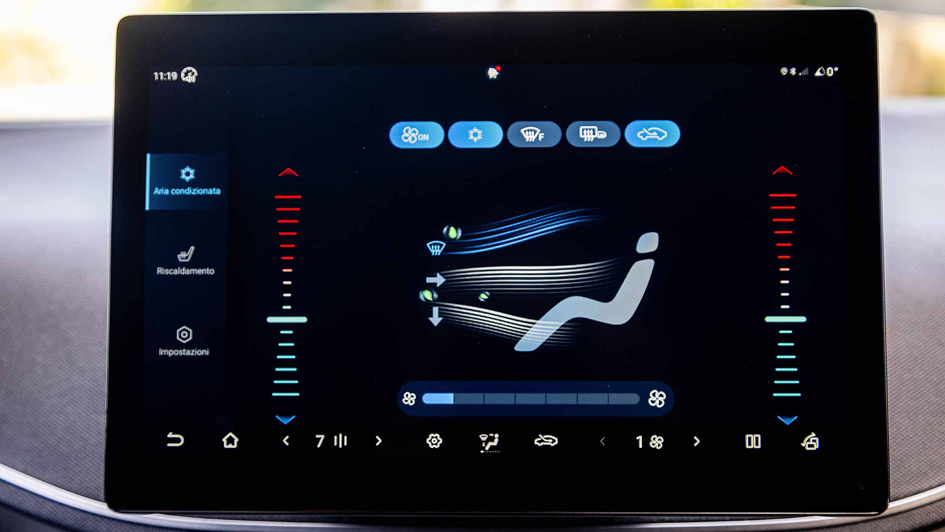A car touchscreen display shows air conditioning controls with icons and settings in Italian. Temperature and airflow adjustments are visible.