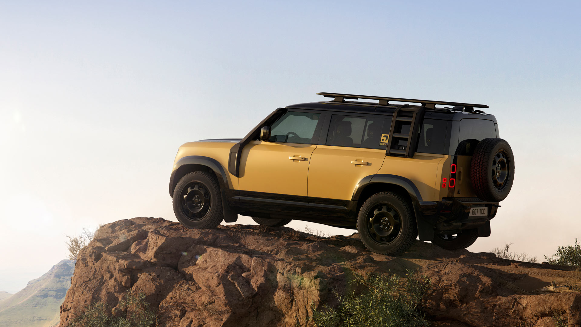A yellow SUV parked on a rocky cliff edge, under clear skies, overlooking distant rolling hills, showcasing adventure and exploration.