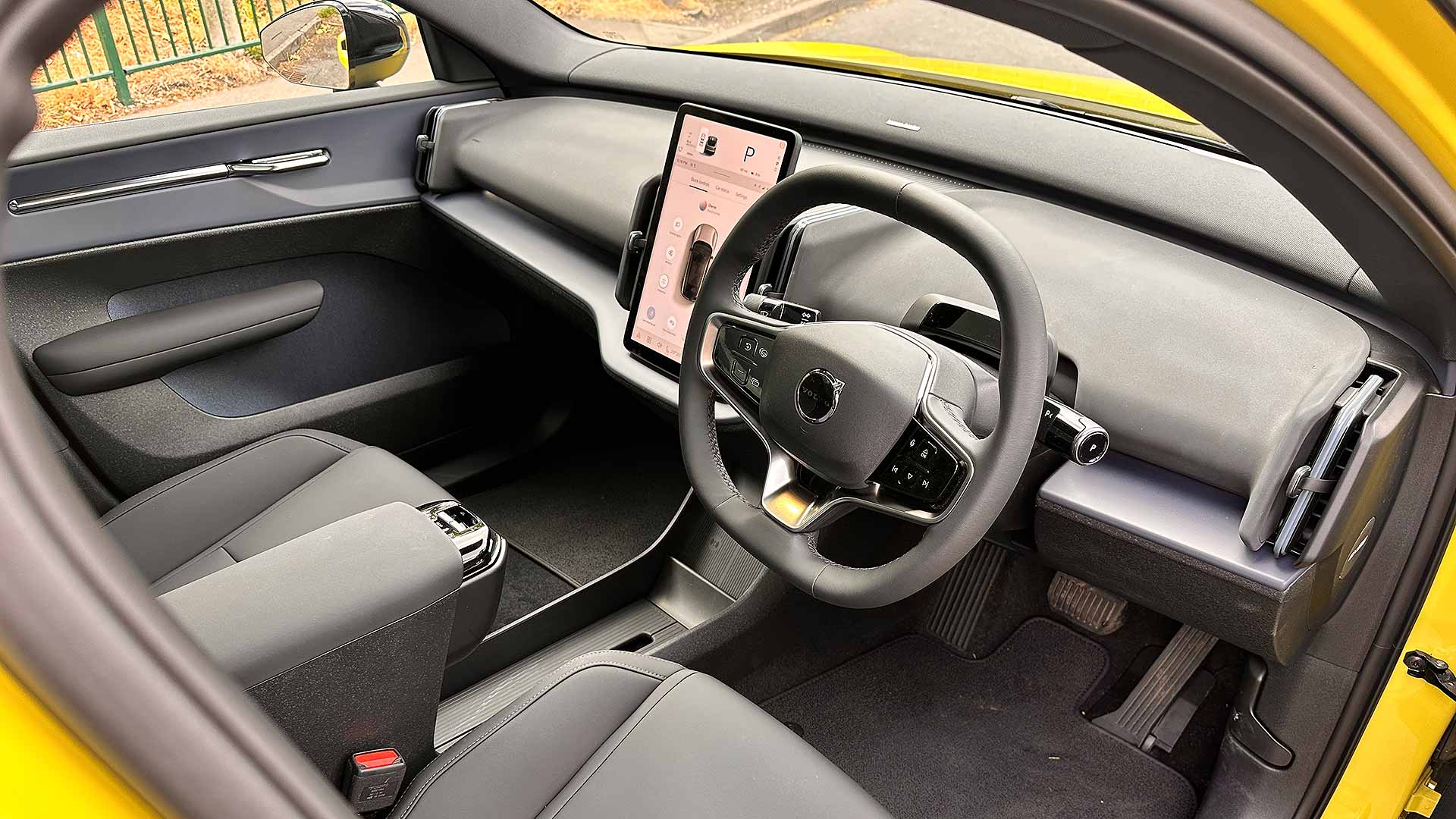 Interior of a yellow car with a modern dashboard, sleek steering wheel, and central touchscreen display, viewed through the open driver’s door.