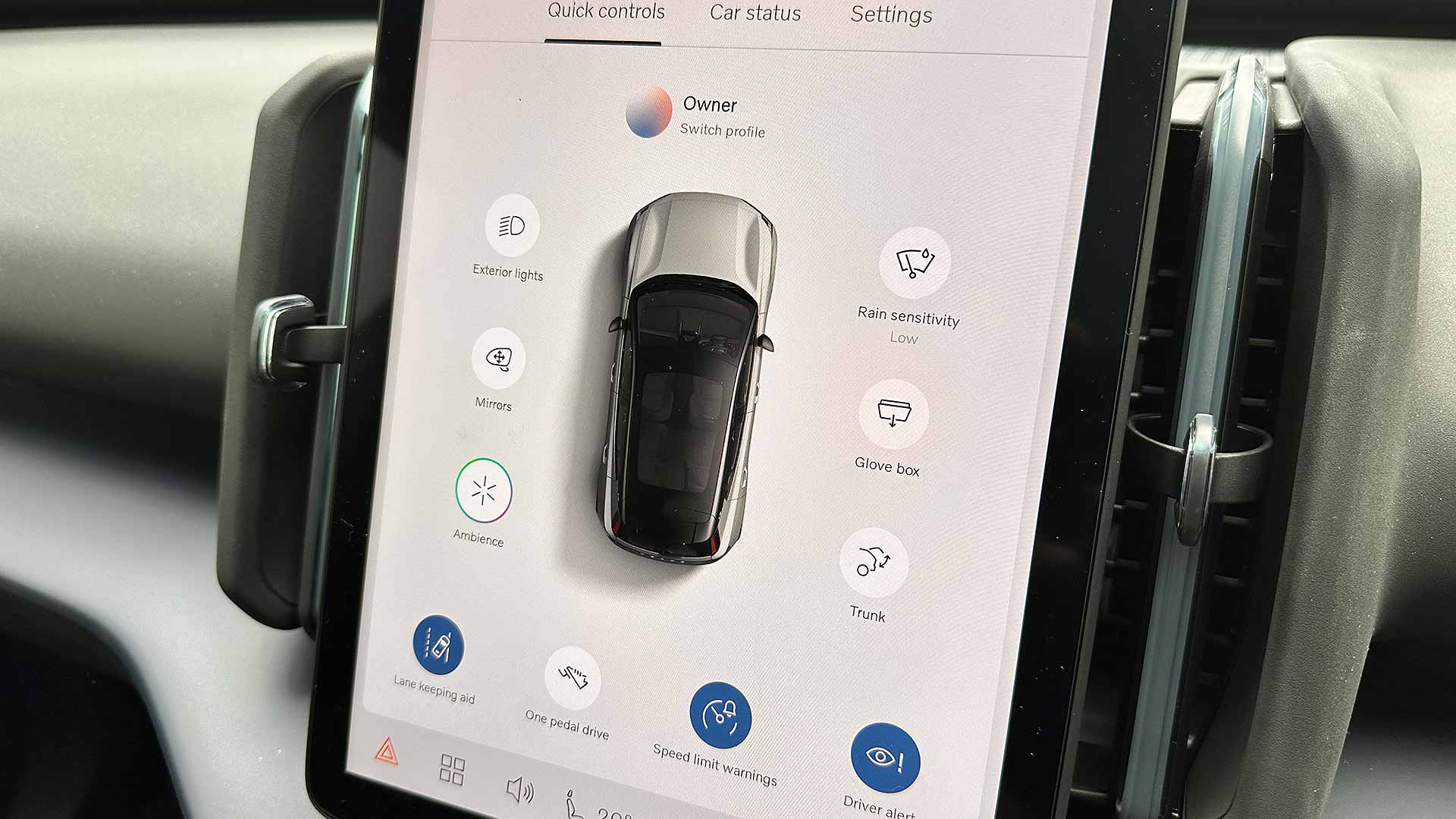 A car's touchscreen display shows vehicle settings and controls, including exterior lights, mirrors, rain sensitivity, glove box, trunk, and ambience options.